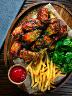 Overhead honey and sriracha glazed chicken wings served with French fries.