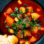 Close-up overhead traditional Hungarian goulash soup or gulyásleves with csipetke (pasta), featuring a title overlay.