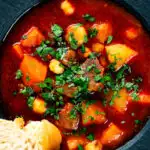 Close-up overhead traditional Hungarian goulash soup or gulyásleves with csipetke (pasta), featuring a title overlay.