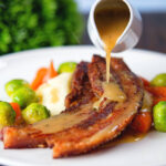 Cider and Bramley apple sauce being poured over cripsy roast pork belly slices.
