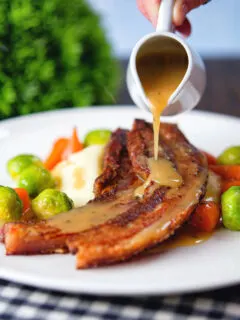 Cider and Bramley apple sauce being poured over cripsy roast pork belly slices.