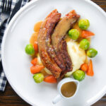 Overhead crispy roast pork belly slices with a cider sauce, mashed potato and veggies.