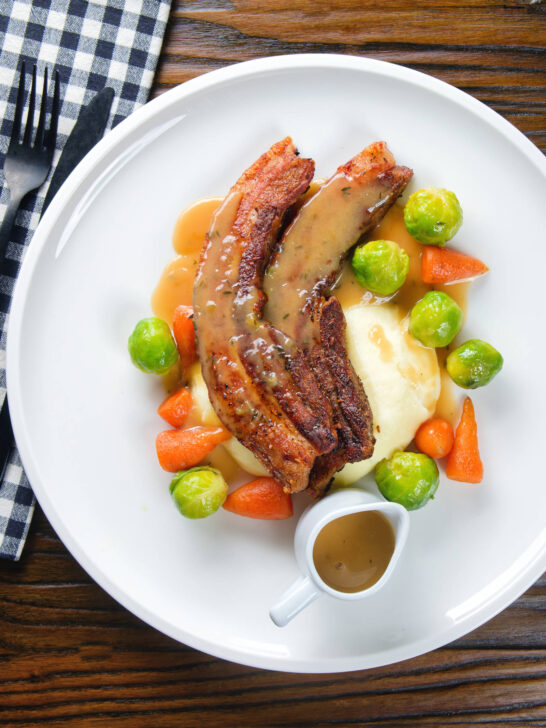 Overhead crispy roast pork belly slices with a cider sauce, mashed potato and veggies.