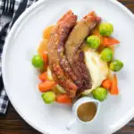 Overhead crispy roast pork belly slices with a cider sauce, mashed potato and veggies.