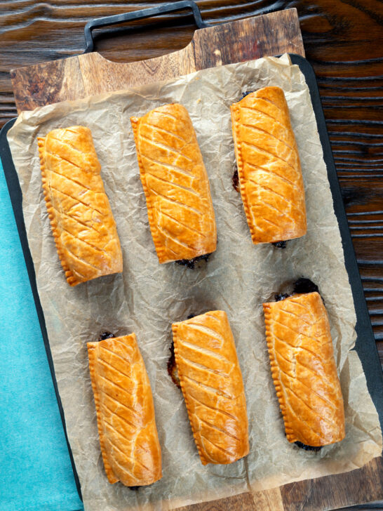 Overhead pork and apple sausage rolls with hot crusty pastry on a baking sheet.