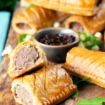 Homemade pork and apple sausage rolls with hot crust pastry cut open to show filling.
