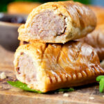 Close-up homemade pork and apple sausage rolls with hot crust pastry cut open to show filling.