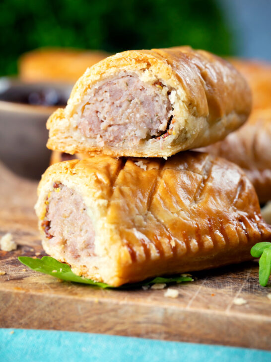 Close-up homemade pork and apple sausage rolls with hot crust pastry cut open to show filling.