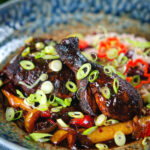 Spicy Jamaican brown stew chicken with spring onions and rice and peas.