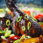 Close-up Jamaican brown stew chicken with spring onions.