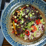 Overhead Jamaican brown stew chicken with spring onions, rice and peas.