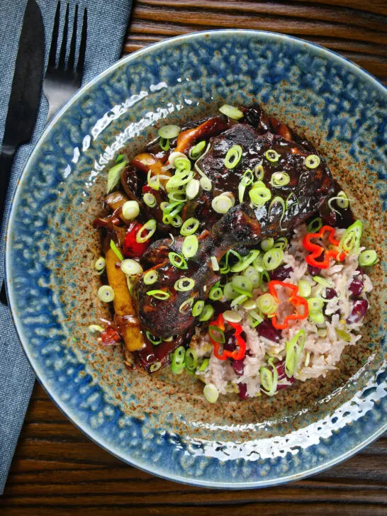 Overhead Jamaican brown stew chicken with spring onions, rice and peas.