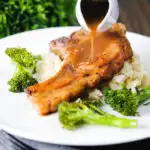 Sauce being poured over brown sugar pork chops served with celeriac mash and broccoli.