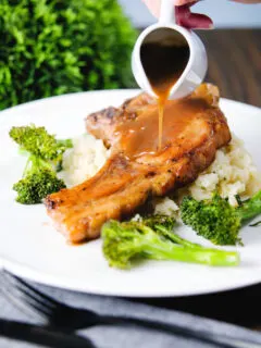 Sauce being poured over brown sugar pork chops served with celeriac mash and broccoli.