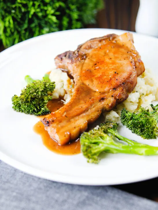 Sauce being poured over brown sugar pork chops served with celeriac mash and broccoli.