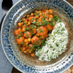 Overhead Indian carrot and chickpeas curry in a thick coconut milk sauce served with coriander rice.