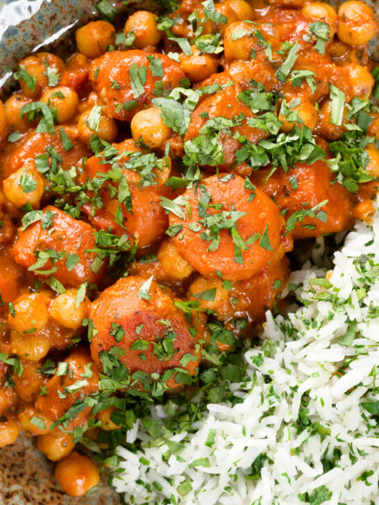 Overhead close-up carrot and chickpeas curry in a thick coconut milk sauce served with coriander rice.