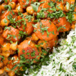 Overhead close-up carrot and chickpeas curry in a thick coconut milk sauce served with coriander rice.