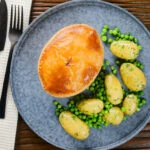 Overhead homemade creamy chicken and bacon pie with peas and buttered potatoes.