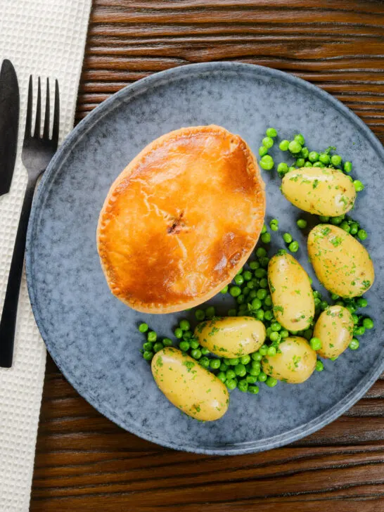 Overhead homemade creamy chicken and bacon pie with peas and buttered potatoes.