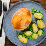 Overhead homemade creamy chicken and bacon pie with peas and buttered potatoes.