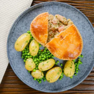 Homemade chicken and bacon pie cut open to show the filling with peas and buttered potatoes.
