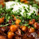 Close-up vegan chickpea and kidney bean chilli served with coriander and vegan sour cream.