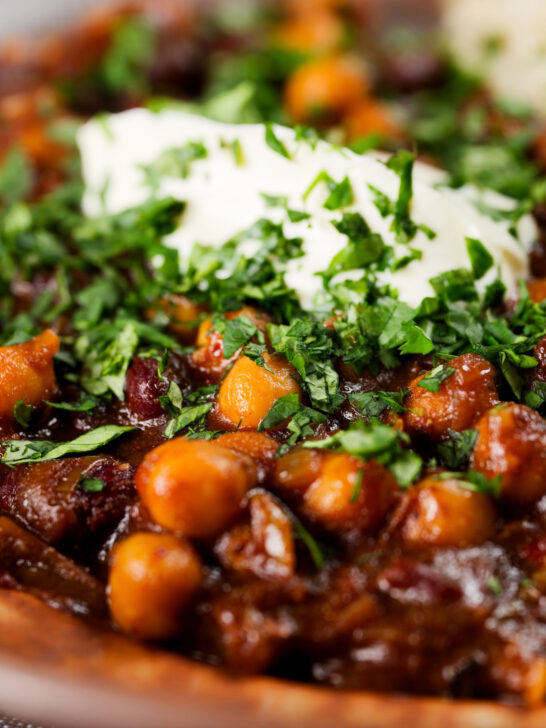 Close-up vegan chickpea and kidney bean chilli served with coriander and vegan sour cream.