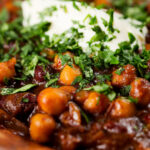 Close-up vegan chickpea and kidney bean chilli served with coriander and vegan sour cream.