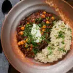 Overhead vegan chickpea and kidney bean chilli served with coriander and rice.