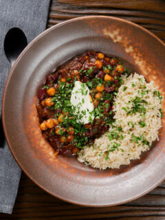 Overhead vegan chickpea and kidney bean chilli served with coriander and rice.