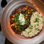 Overhead vegan chickpea and kidney bean chilli served with coriander and rice.