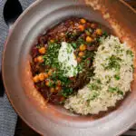 Overhead vegan chickpea and kidney bean chilli served with coriander and rice.