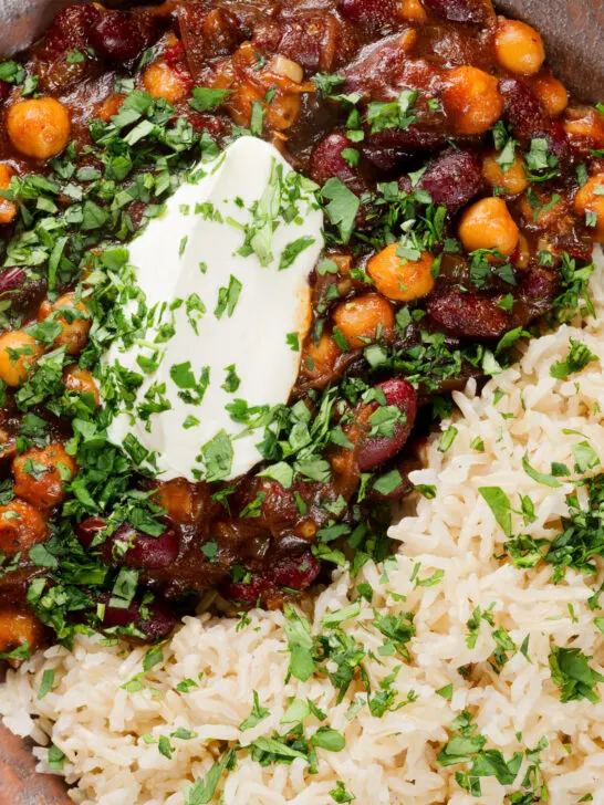 Overhead close-up vegan chickpea and kidney bean chilli served with coriander and rice.