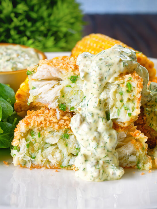 Homemade baked crab cakes cut open to show texture served with tartar sauce.