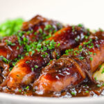 Close-up devilled sausages in a spicy onion gravy with mashed potato and peas.