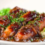 Close-up devilled sausages in a spicy onion gravy with mashed potato and peas.