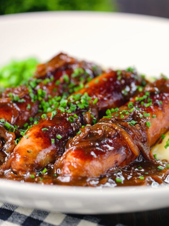 Close-up devilled sausages in a spicy onion gravy with mashed potato and peas.