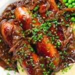 Overhead close-up devilled sausages in a spicy onion gravy with mashed potato and peas.