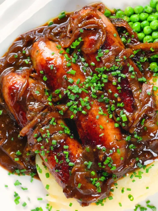 Overhead close-up devilled sausages in a spicy onion gravy with mashed potato and peas.