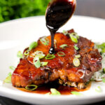 Filipino adobo sauce being poured over glazed pork chops served with rice.