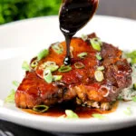 Filipino adobo sauce being poured over glazed pork chops served with rice.