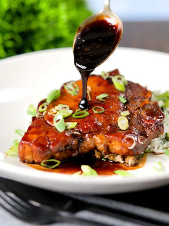 Filipino adobo sauce being poured over glazed pork chops served with rice.