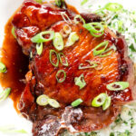 Cloe-up overhead Filipino-inspired adobo pork chops served with rice and spring onions.