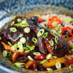 Spicy Jamaican brown stew chicken with spring onions and rice and peas.