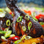 Close-up Jamaican brown stew chicken with spring onions.