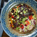 Overhead Jamaican brown stew chicken with spring onions, rice and peas.
