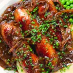 Overhead close-up devilled sausages in a spicy onion gravy with mashed potato and peas.