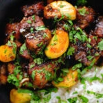 Close-up overhead pork belly curry with tamarind, black pepper and whole garlic cloves served with rice.