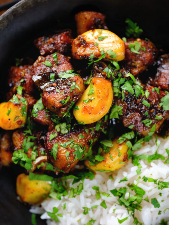 Close-up overhead pork belly curry with tamarind, black pepper and whole garlic cloves served with rice.